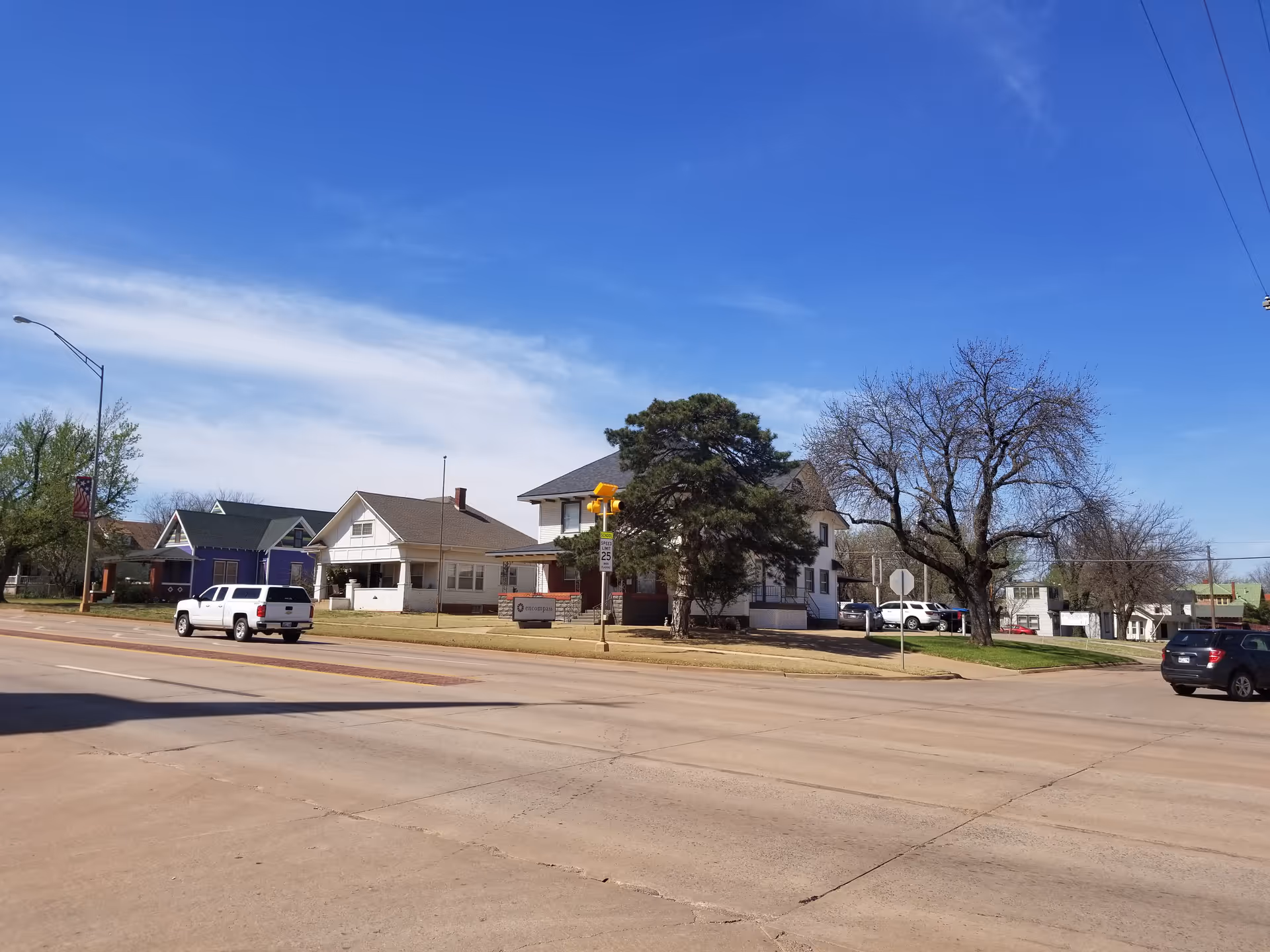 Exterior view of a quiet residential street with houses, trees, and blue sky.