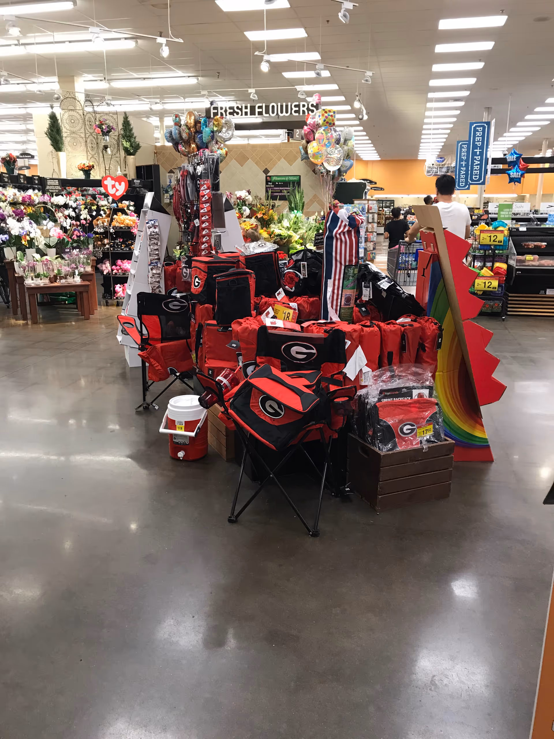 Indoor supermarket scene with flower displays, balloons, and folding chairs.