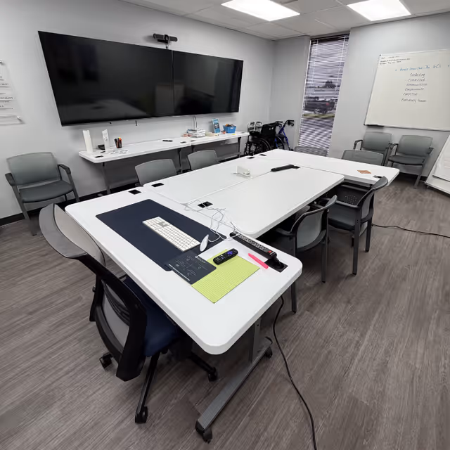 A bright, modern meeting room with a large TV, white tables, and chairs.