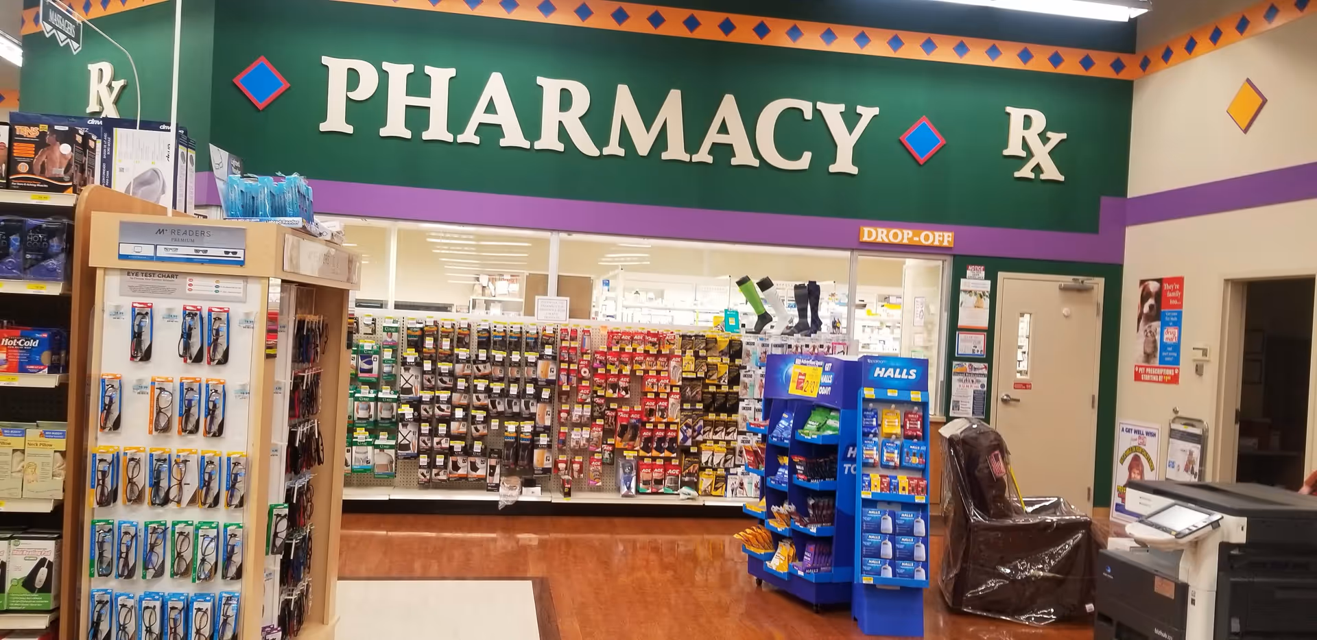 Green-walled pharmacy counter area with shelves of medicines and a PHARMACY sign at Discount Drug Mart.