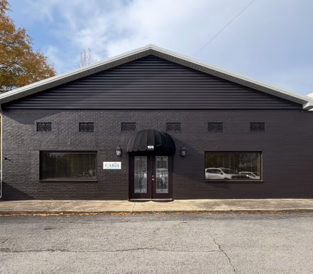 Single-story dark brick building with black awning over double doors and Caris signage.