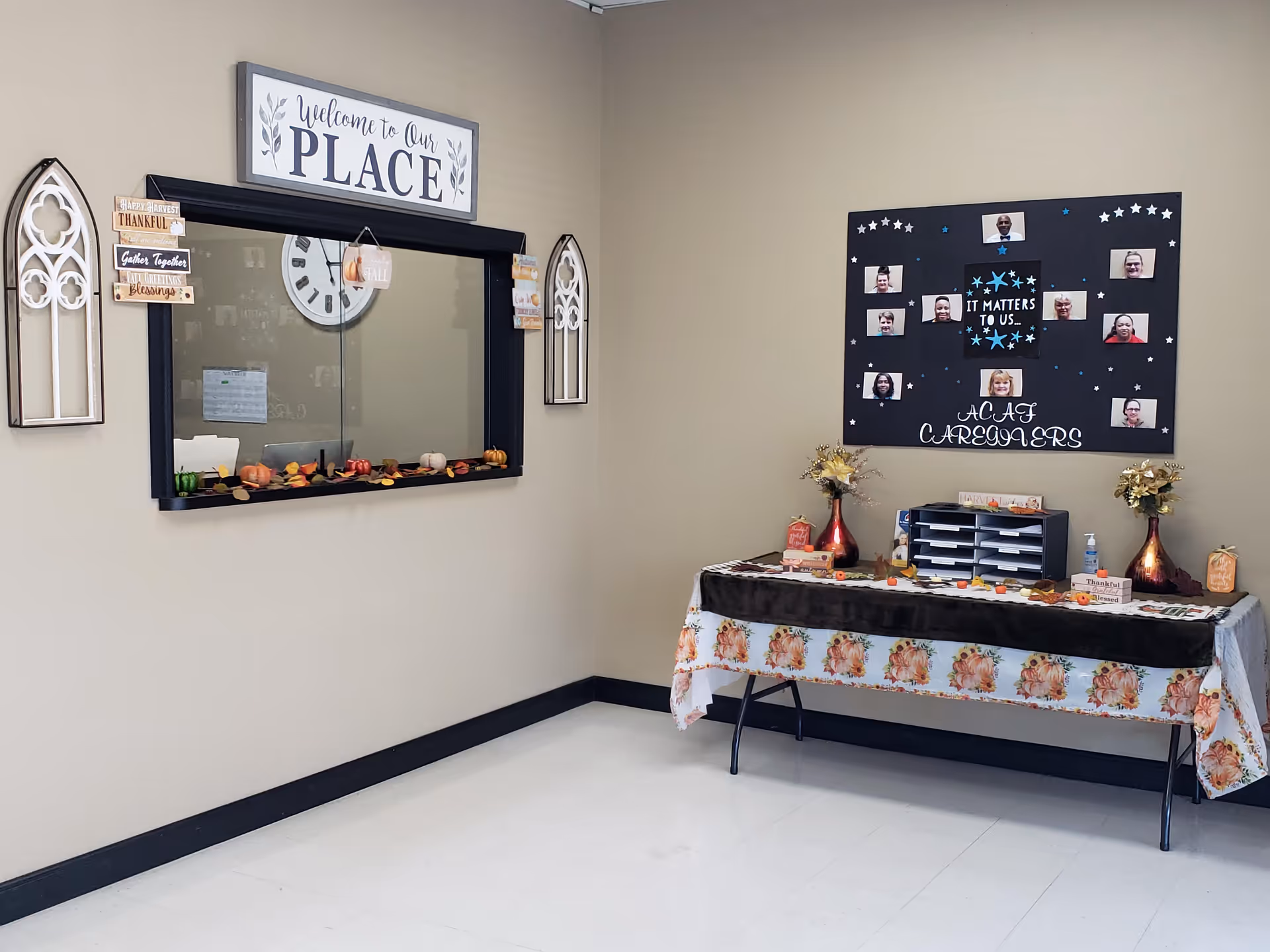 A beige-walled reception area with a window, a floral table display, and a community board.