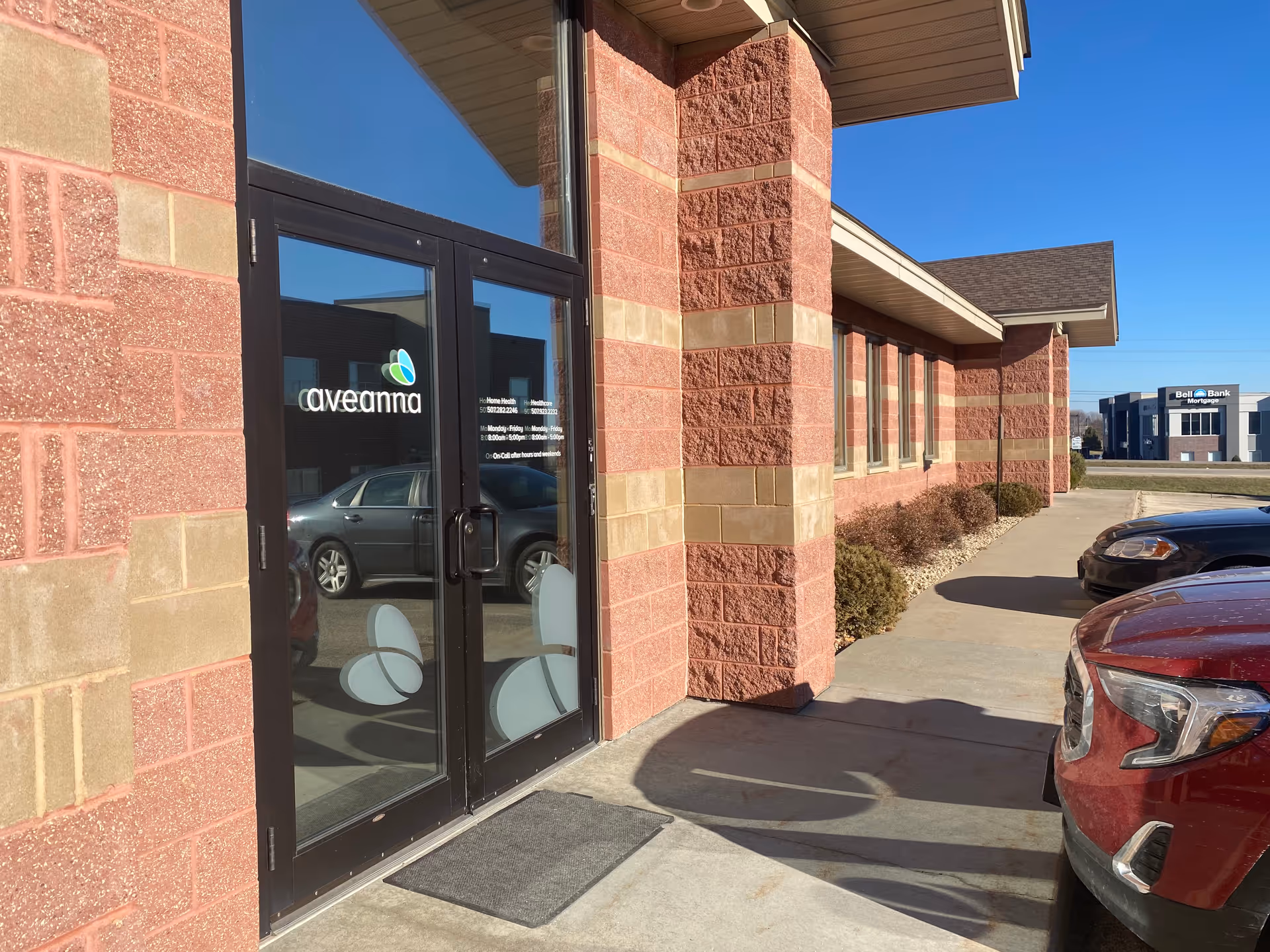 Exterior view of Aveanna Home Health entrance with glass doors and parked cars.
