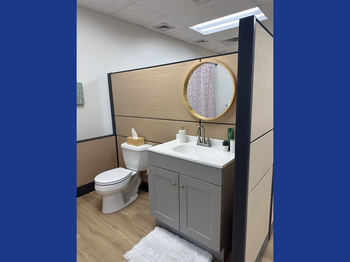 Bathroom area with toilet, vanity, round mirror, and partitioned walls.
