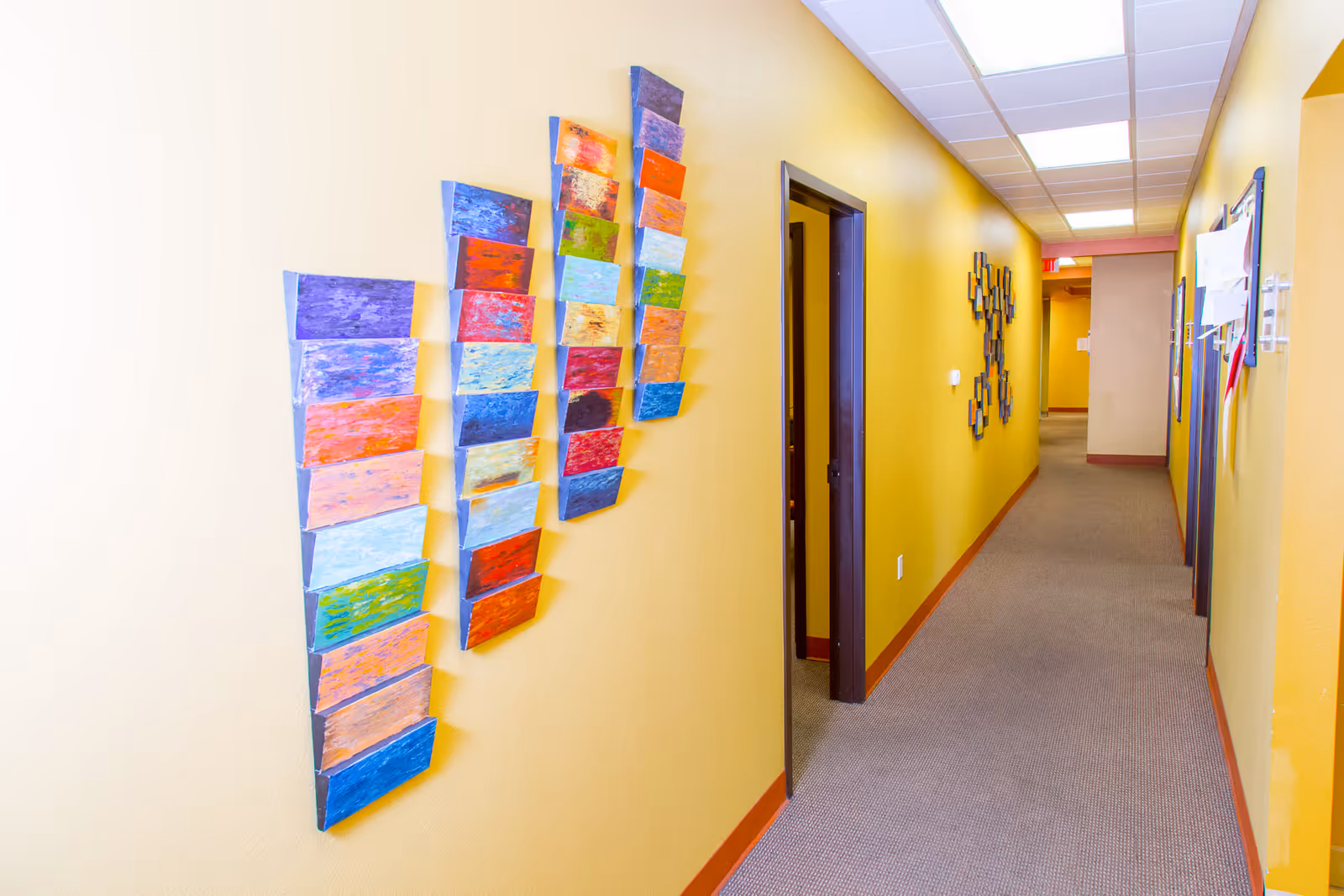 Bright yellow hallway in a senior care facility with colorful wall art and closed doors.