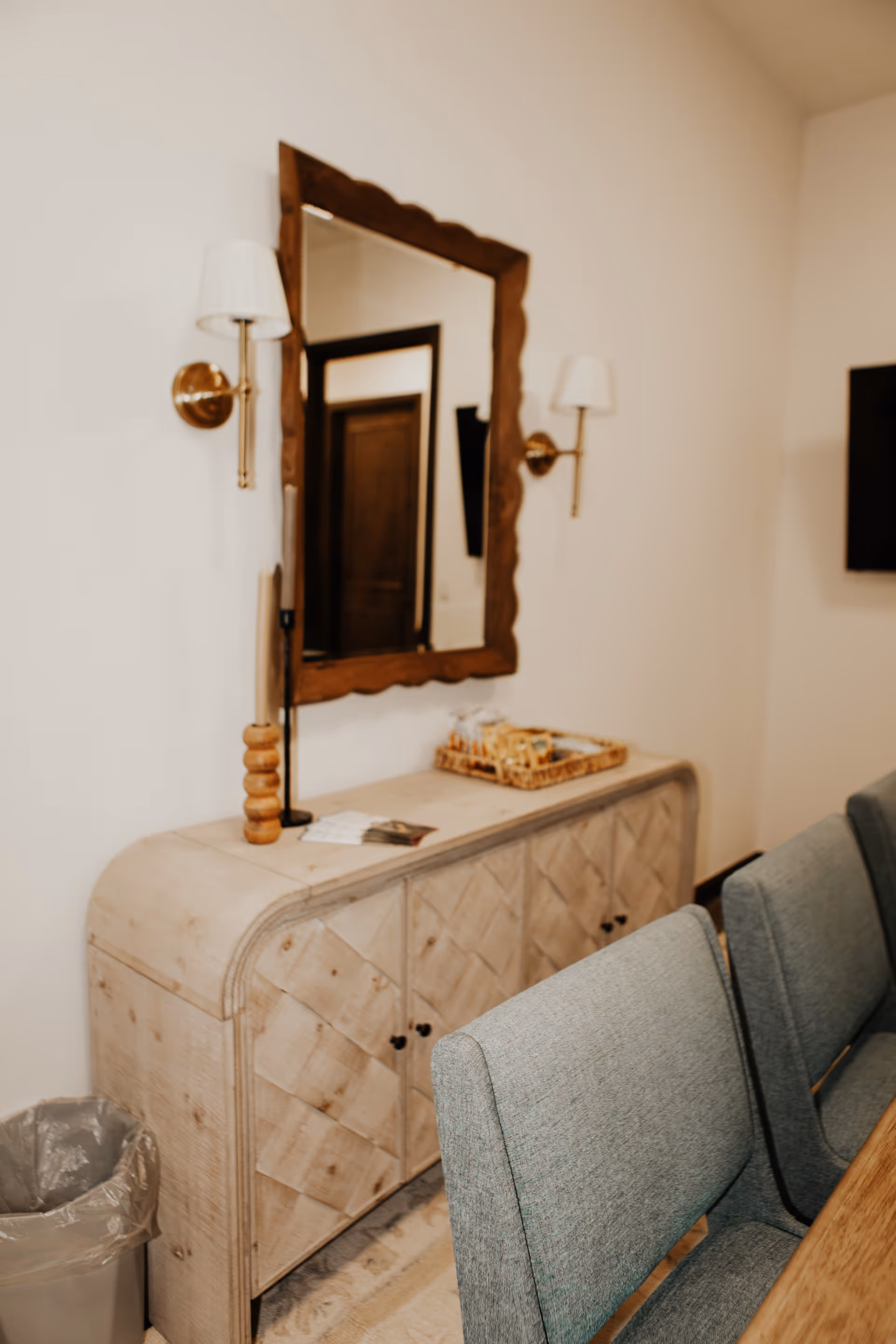 Cozy dining area featuring a wooden console, large mirror, wall sconces, and blue upholstered chairs.
