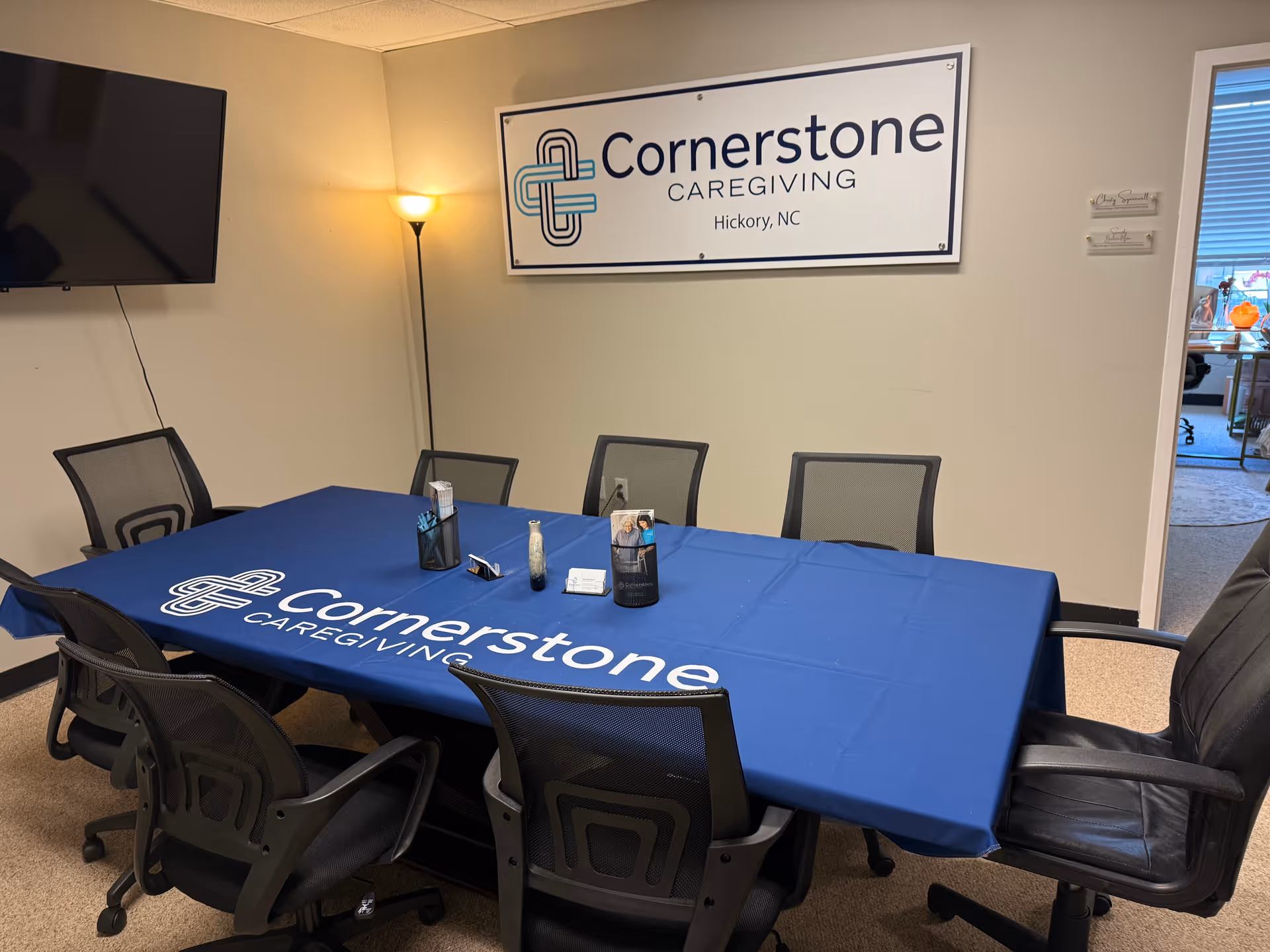 A conference room with a blue Cornerstone Caregiving tablecloth and wall sign.