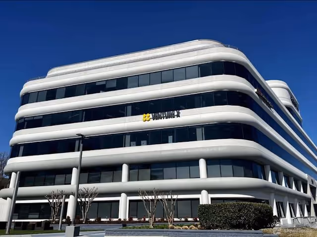 Modern curved white office building with multiple glass windows and trimmed landscaping.