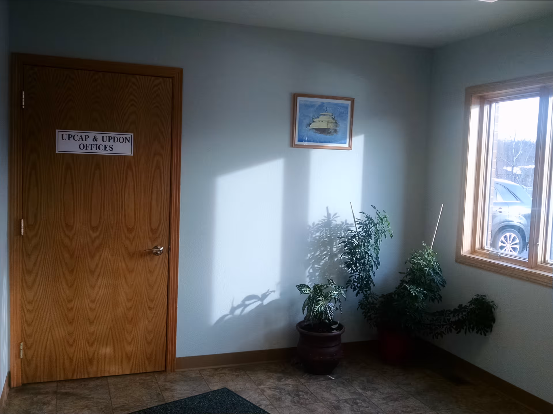 Wooden office door labeled UPCAP & UPDON OFFICES beside potted plants by a window.