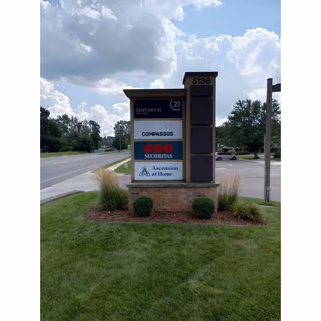 Outdoor brick sign displaying Compassus and partner company logos beside a grassy landscape