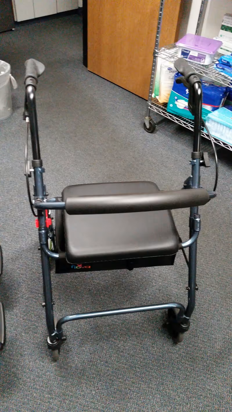 A wheeled walker rests on carpeted floor beside a rolling shelf in a storage area.