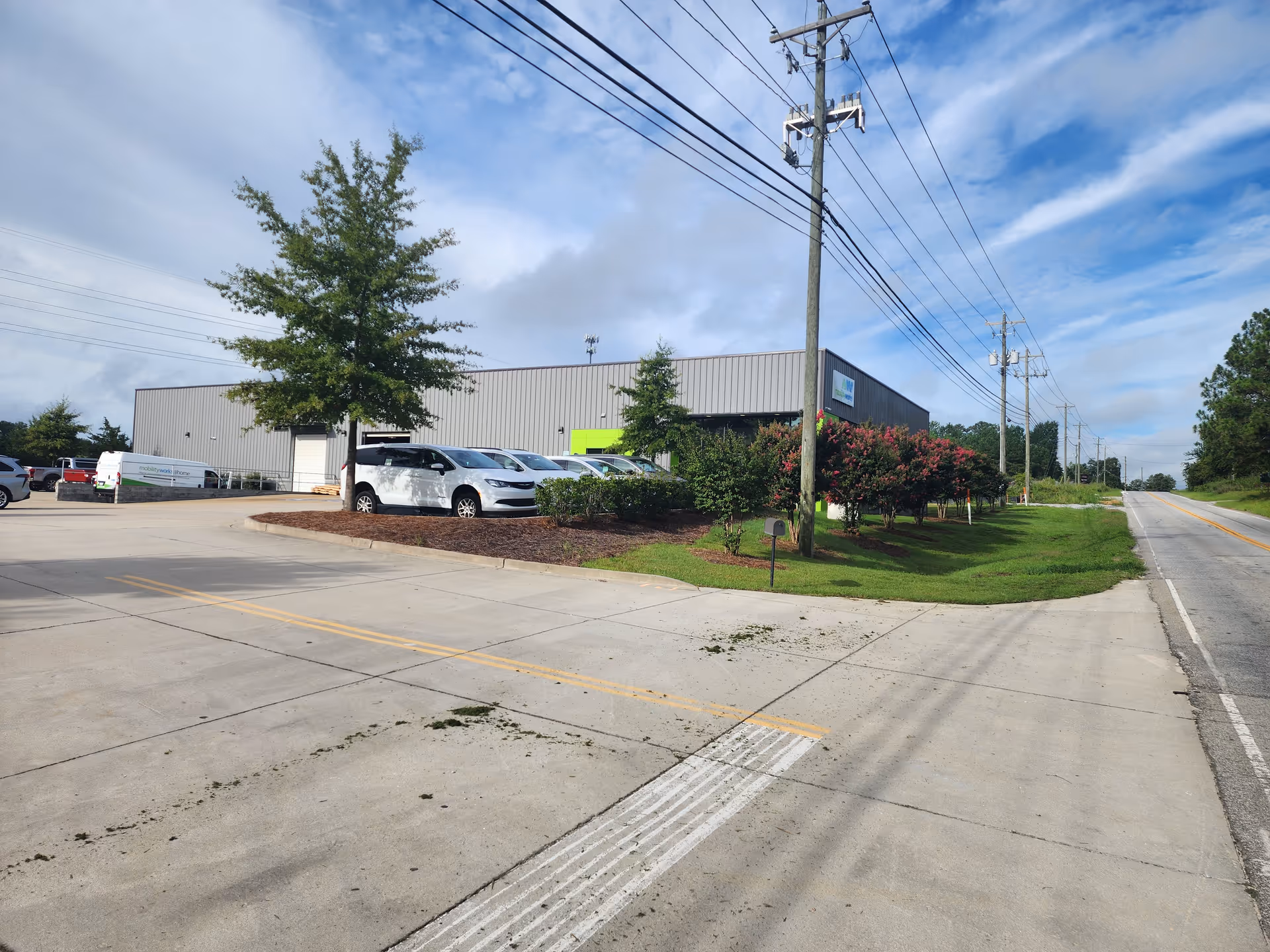 Exterior view of MobilityWorks facility with parking and landscaped greenery along a road.