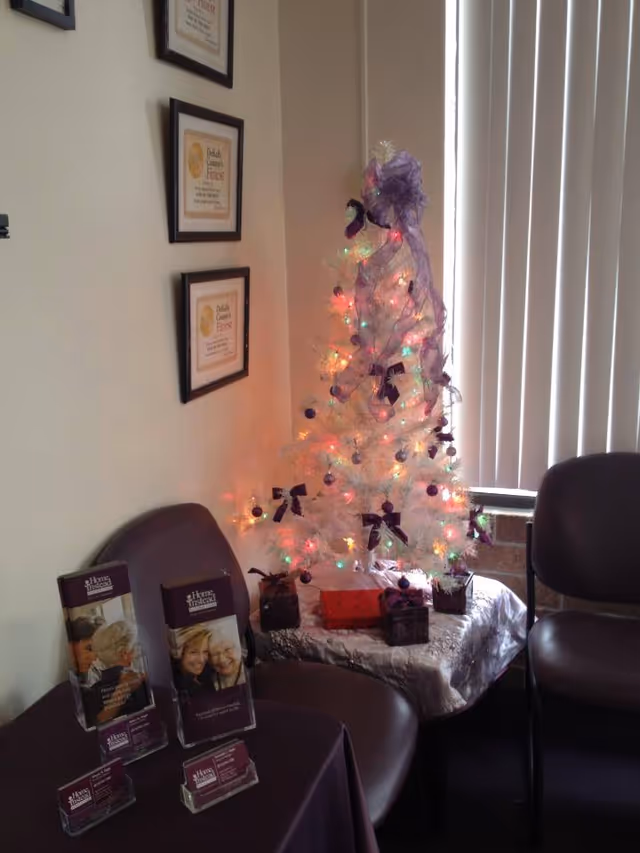 A white Christmas tree with lights and purple bows sits on a table in a lobby.