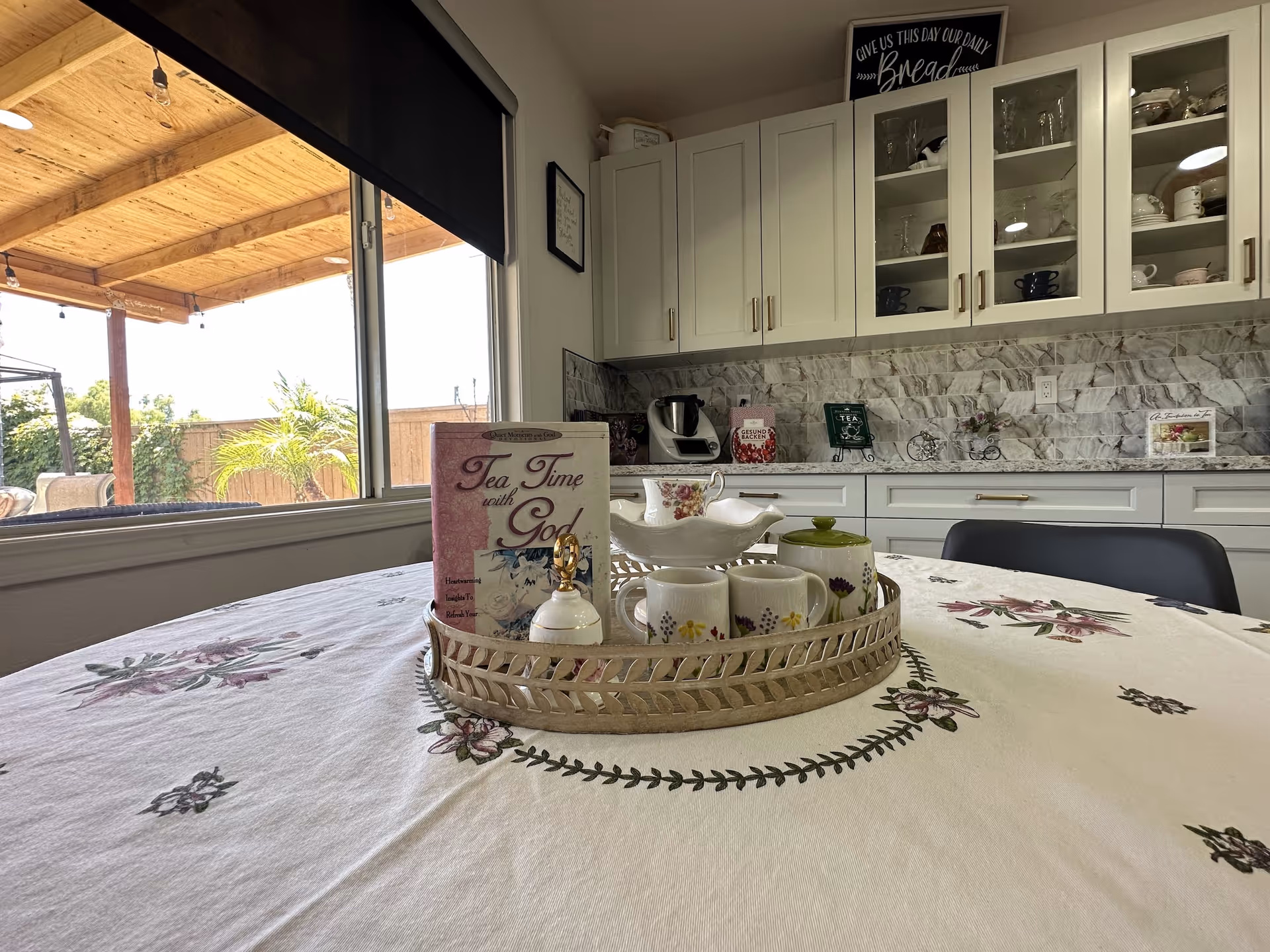 A bright kitchen-dining area with white cabinets, stone backsplash, and a round table set for tea.