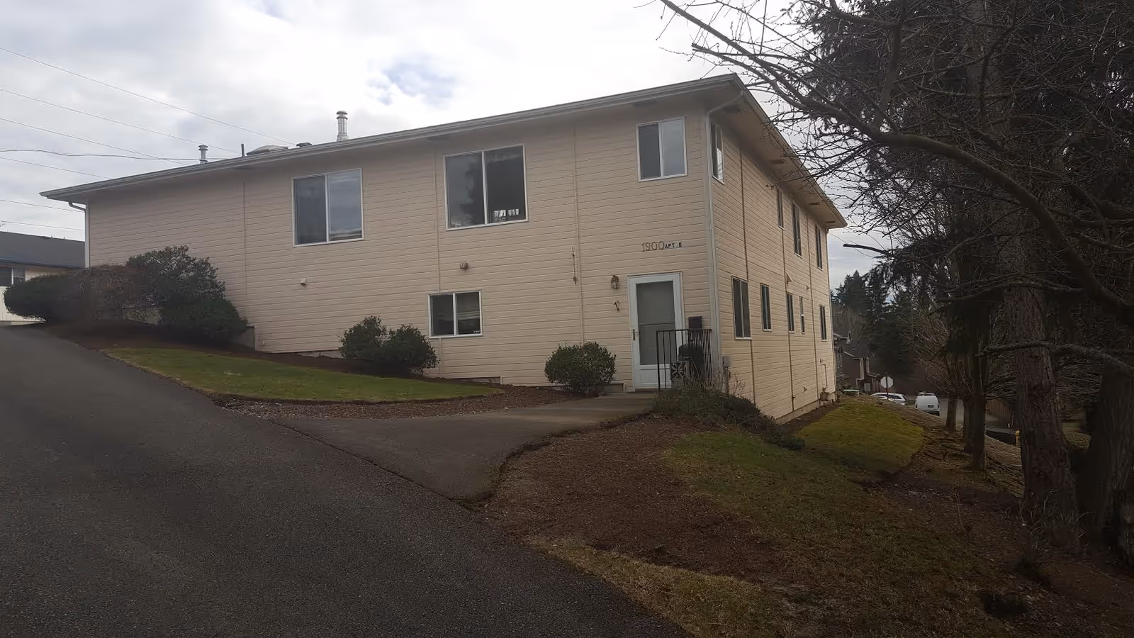 Beige two-story senior living facility exterior with a sloped driveway and trees.