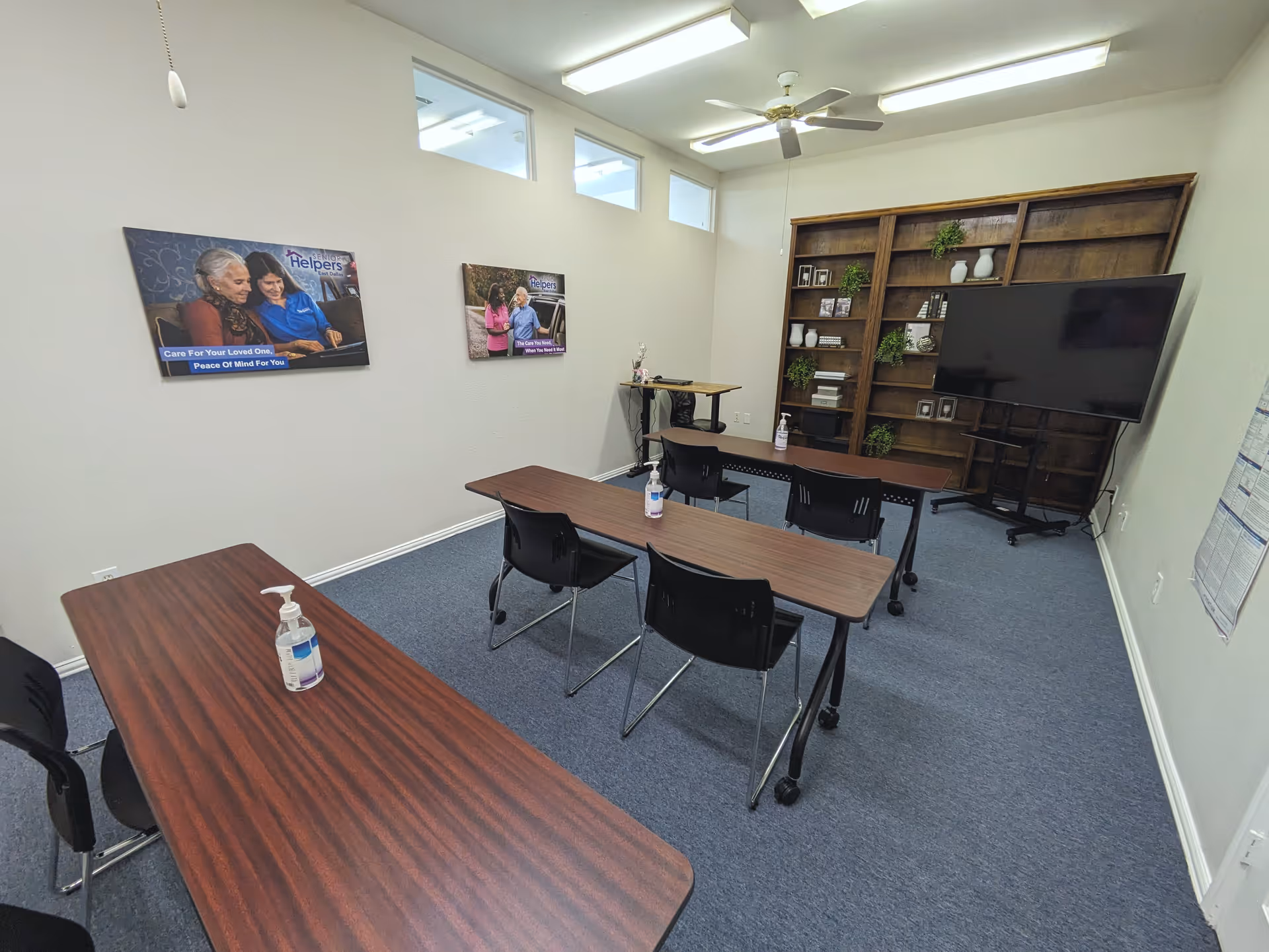 A small meeting room with tables, chairs, a large TV, and a bookshelf.