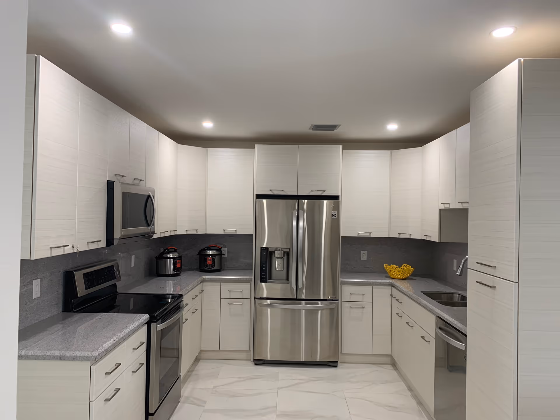 Modern white kitchen with stainless steel appliances and grey countertops.