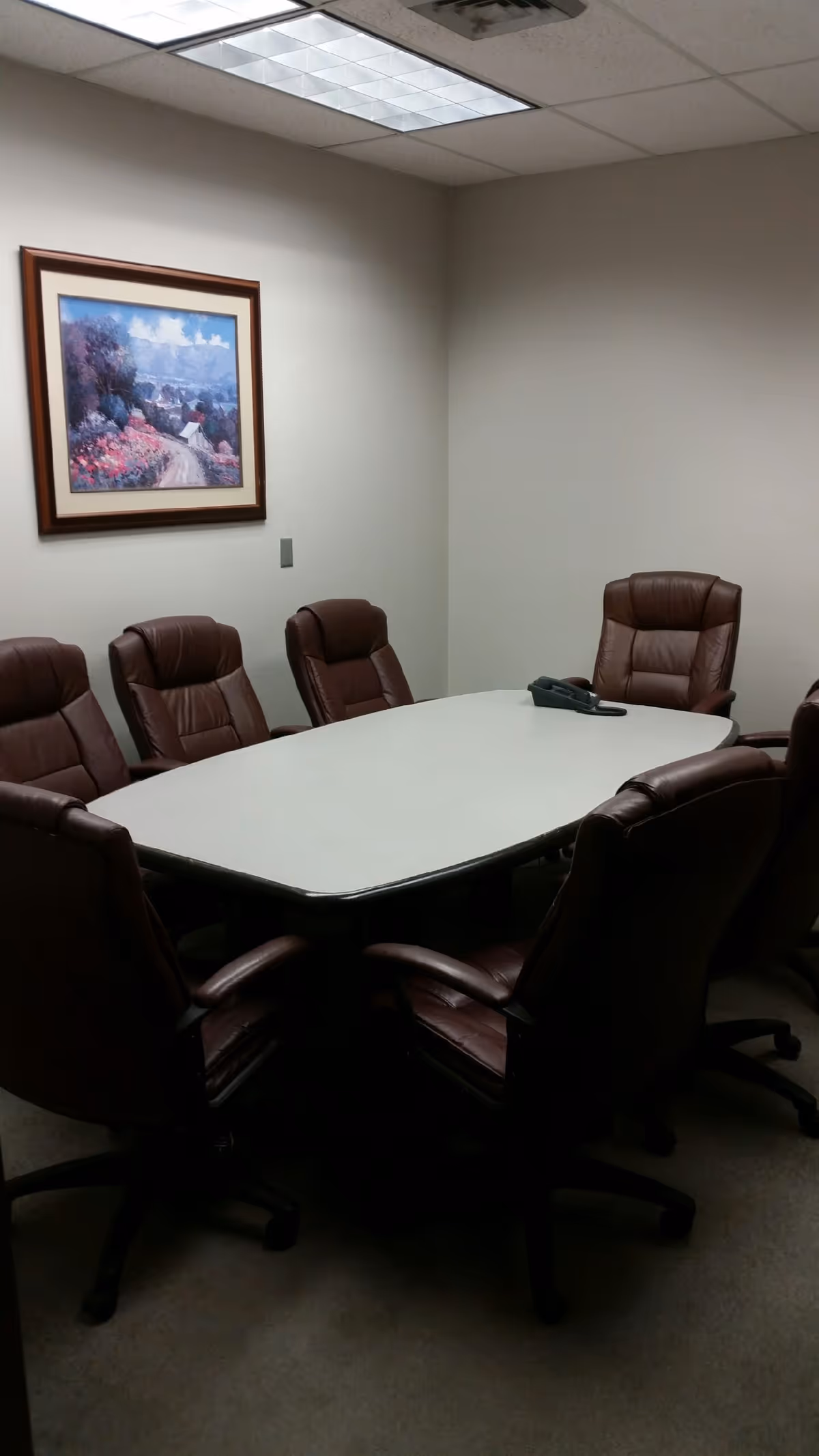 A conference room with a large oval table surrounded by brown leather chairs.
