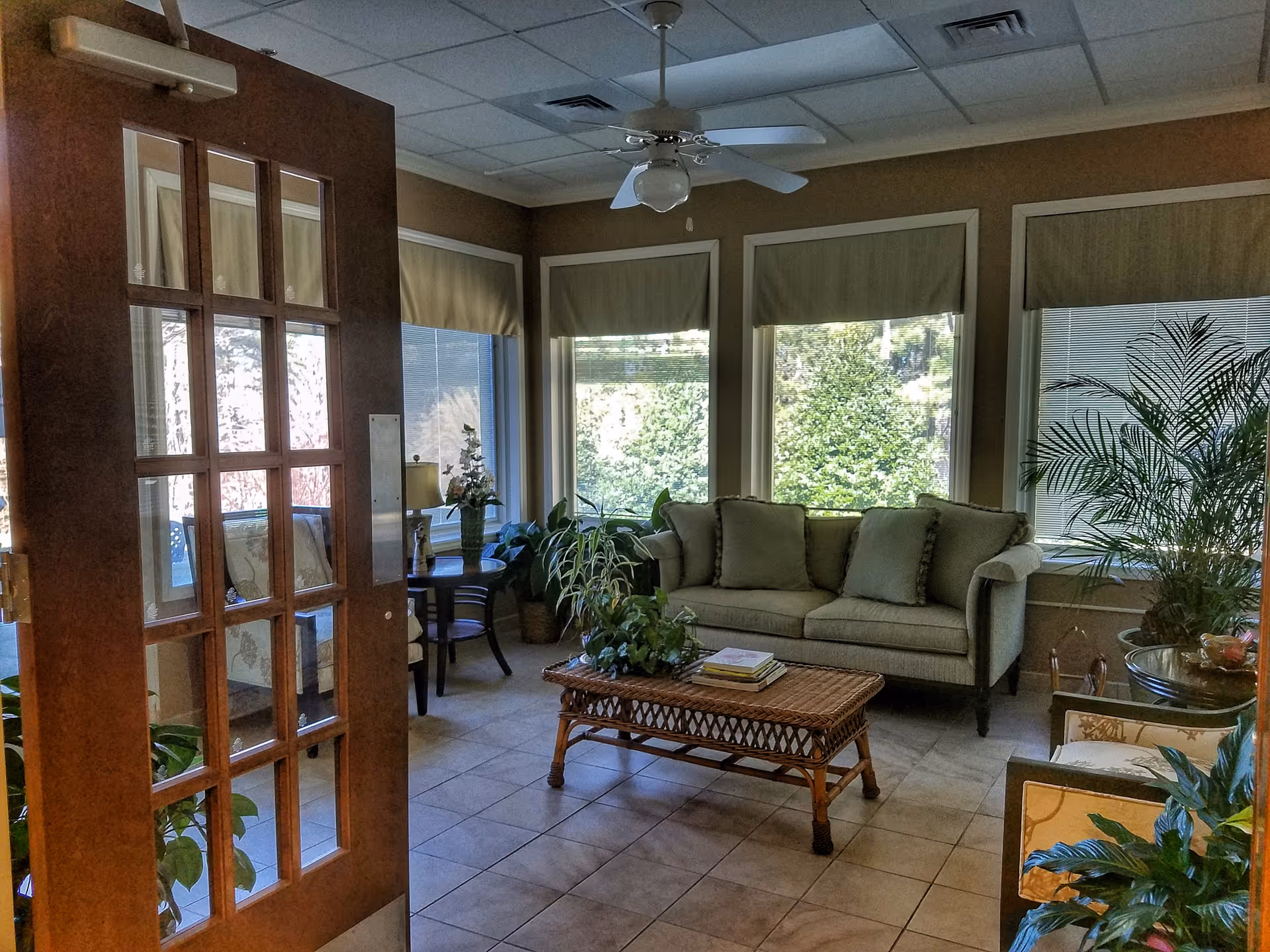 Cozy living room lounge with sofa, plants, coffee table, and large windows.