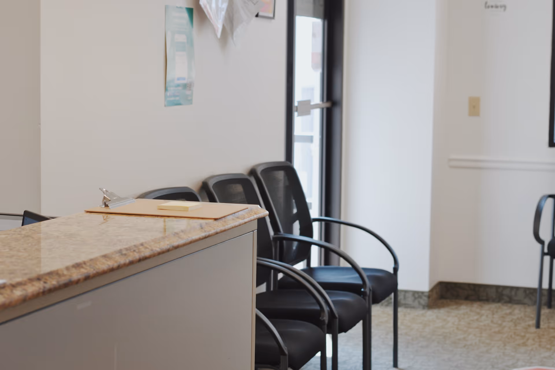 Interior reception area with a granite desk and row of black waiting chairs.