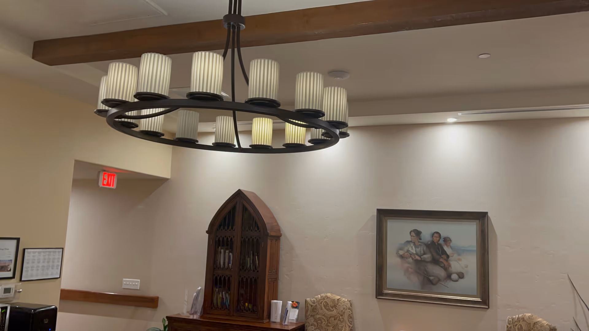 Interior lounge area with circular chandelier, wooden cabinet, framed painting, and beige walls.