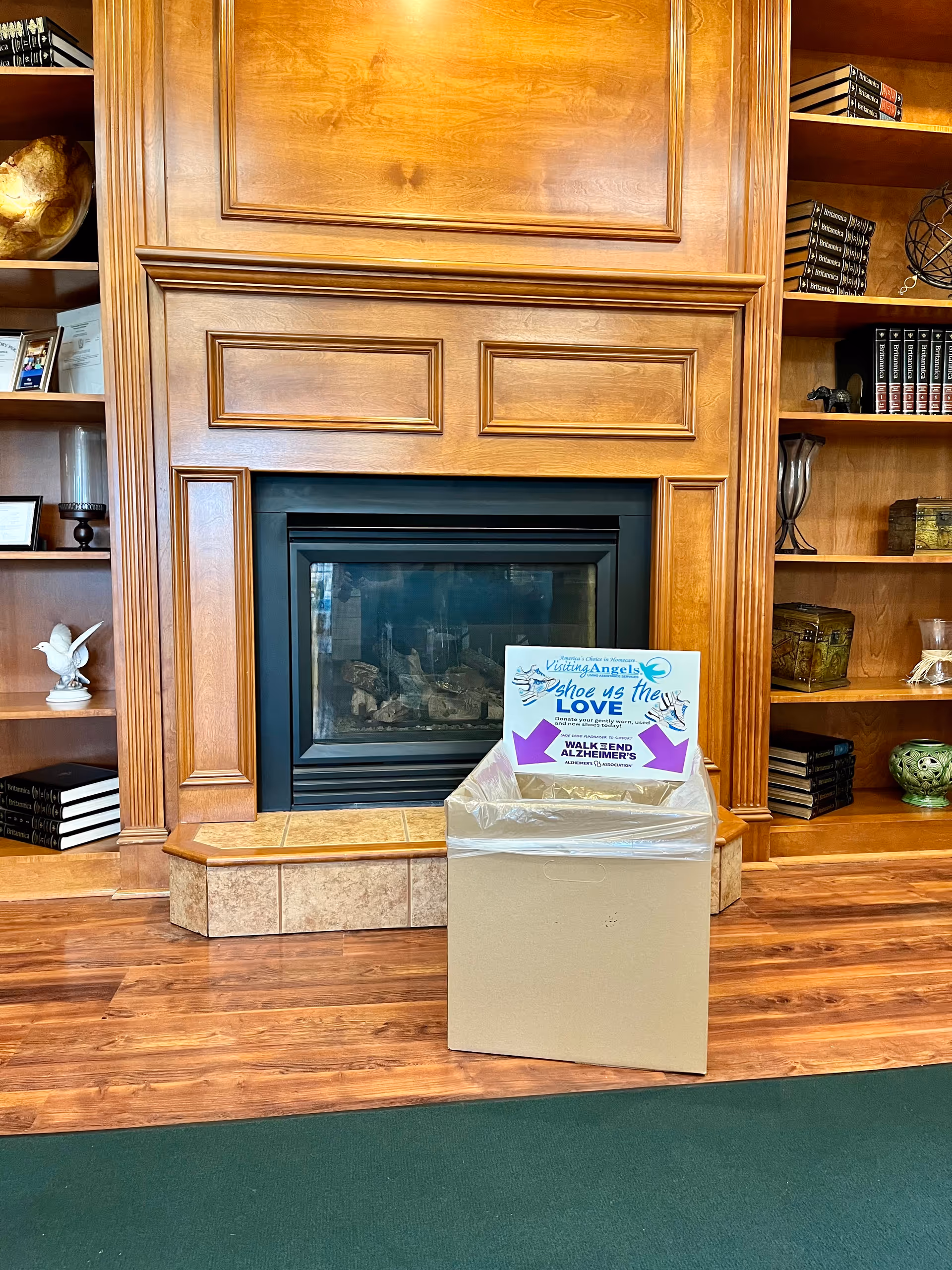 Wood-paneled fireplace flanked by shelves and a donation box inside a senior facility.