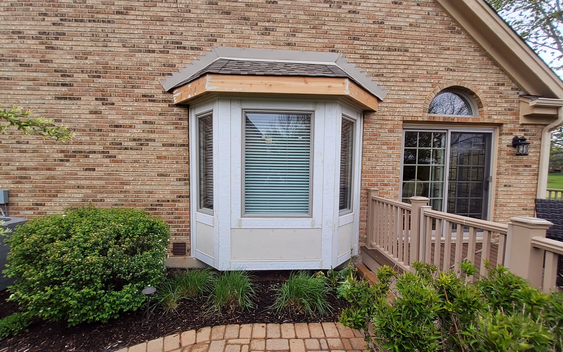 Brick senior living facility exterior with a bay window, sliding door, and wooden railing.