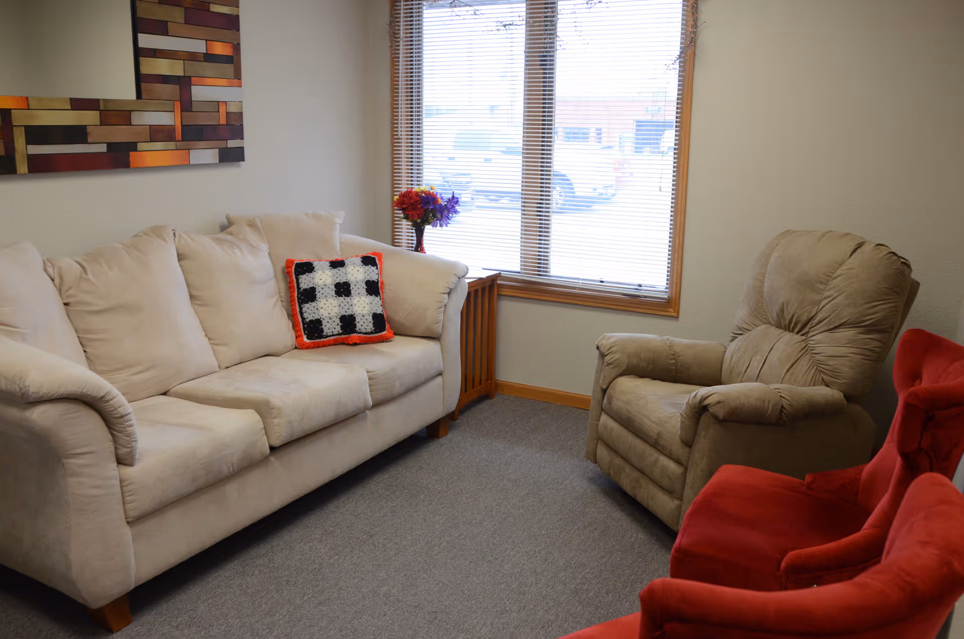 Cozy beige living room with sofa, armchairs, window, and a vase of flowers.