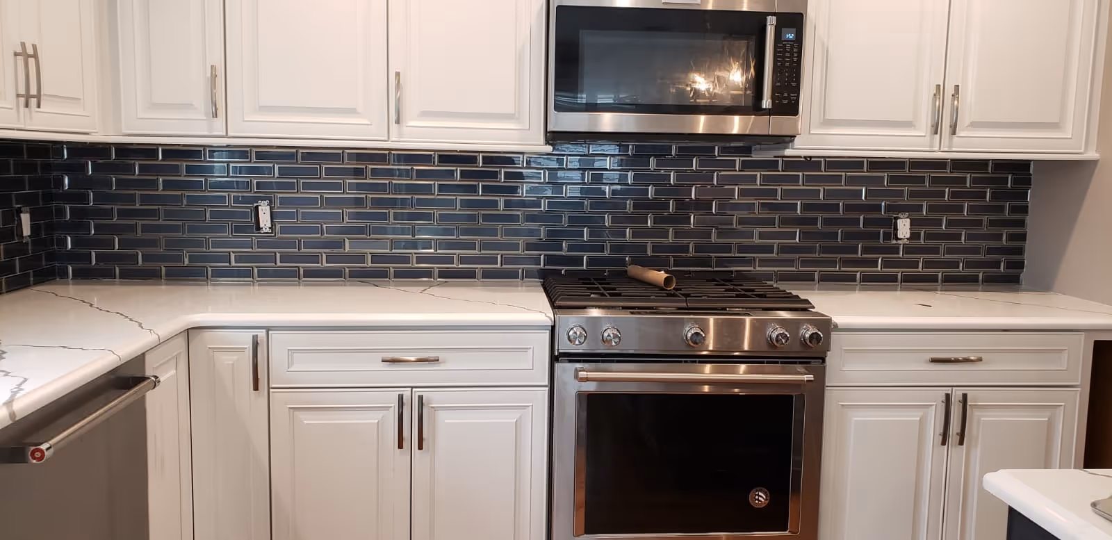 White kitchen with stainless steel stove, microwave, blue tile backsplash, and white cabinets.