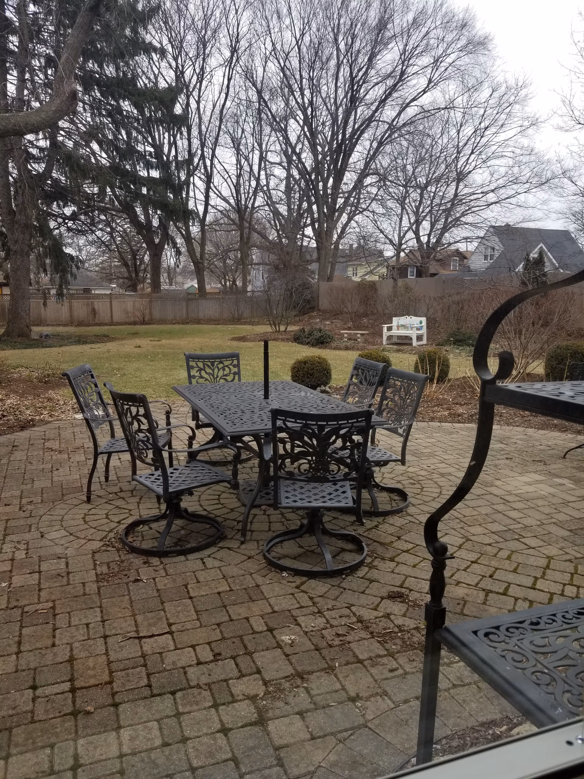 Metal patio table and chairs on a brick courtyard with leafless trees in background.
