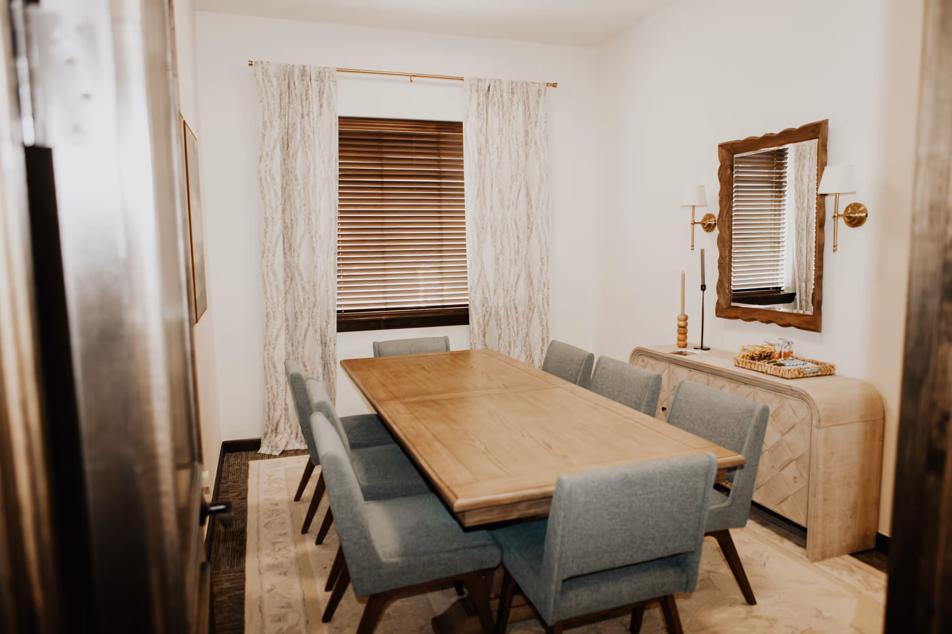 A dining room with a long wooden table, teal chairs, curtains, and a sideboard.