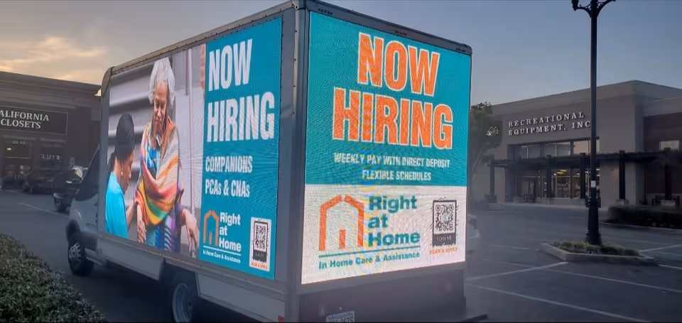 A Right at Home truck displays Now Hiring ads in a parking lot.