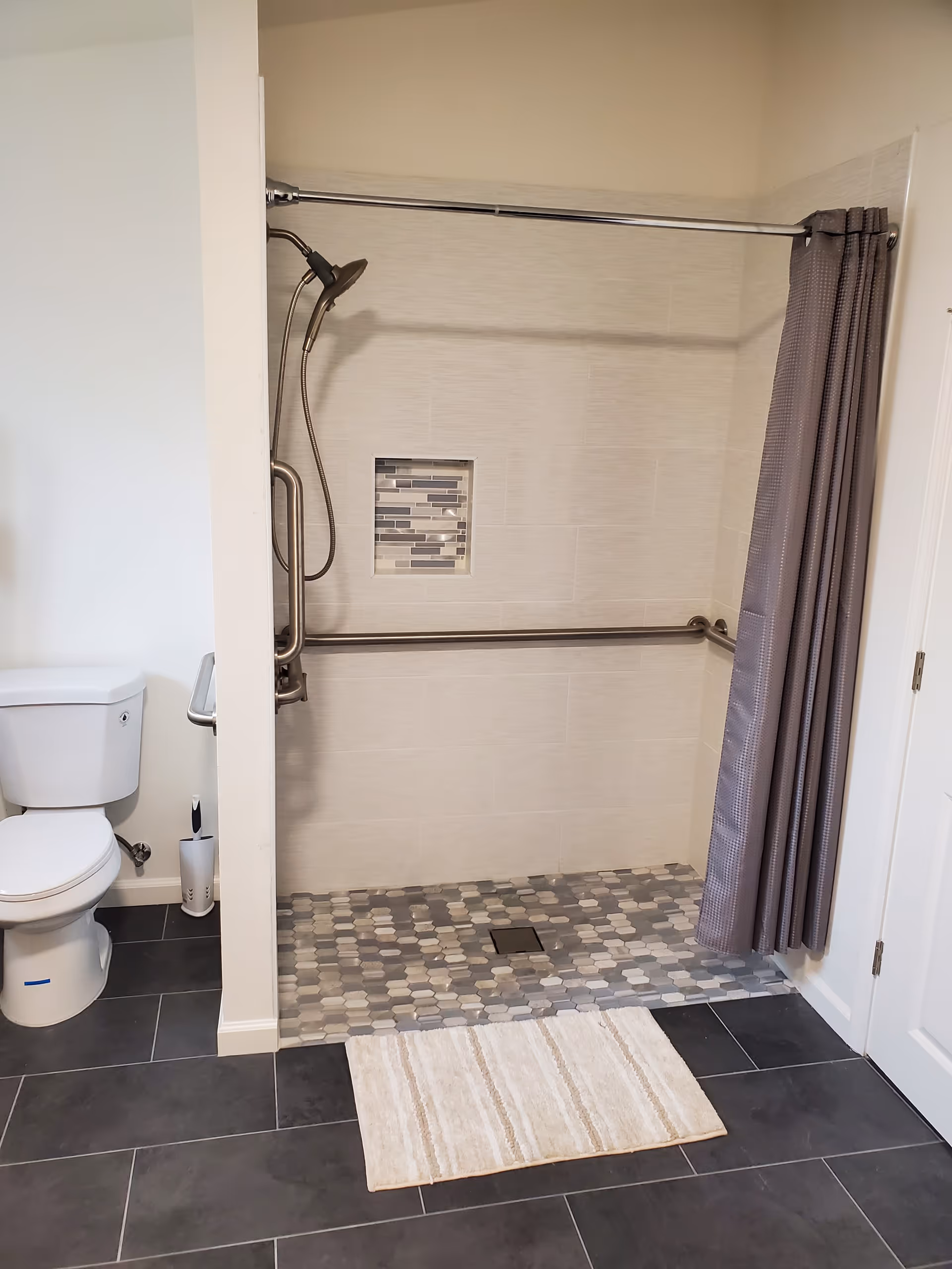Accessible bathroom featuring a walk-in tiled shower with grab bars and a toilet.