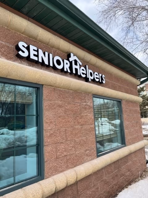 Exterior view of a Senior Helpers building sign on brick wall beside windows.