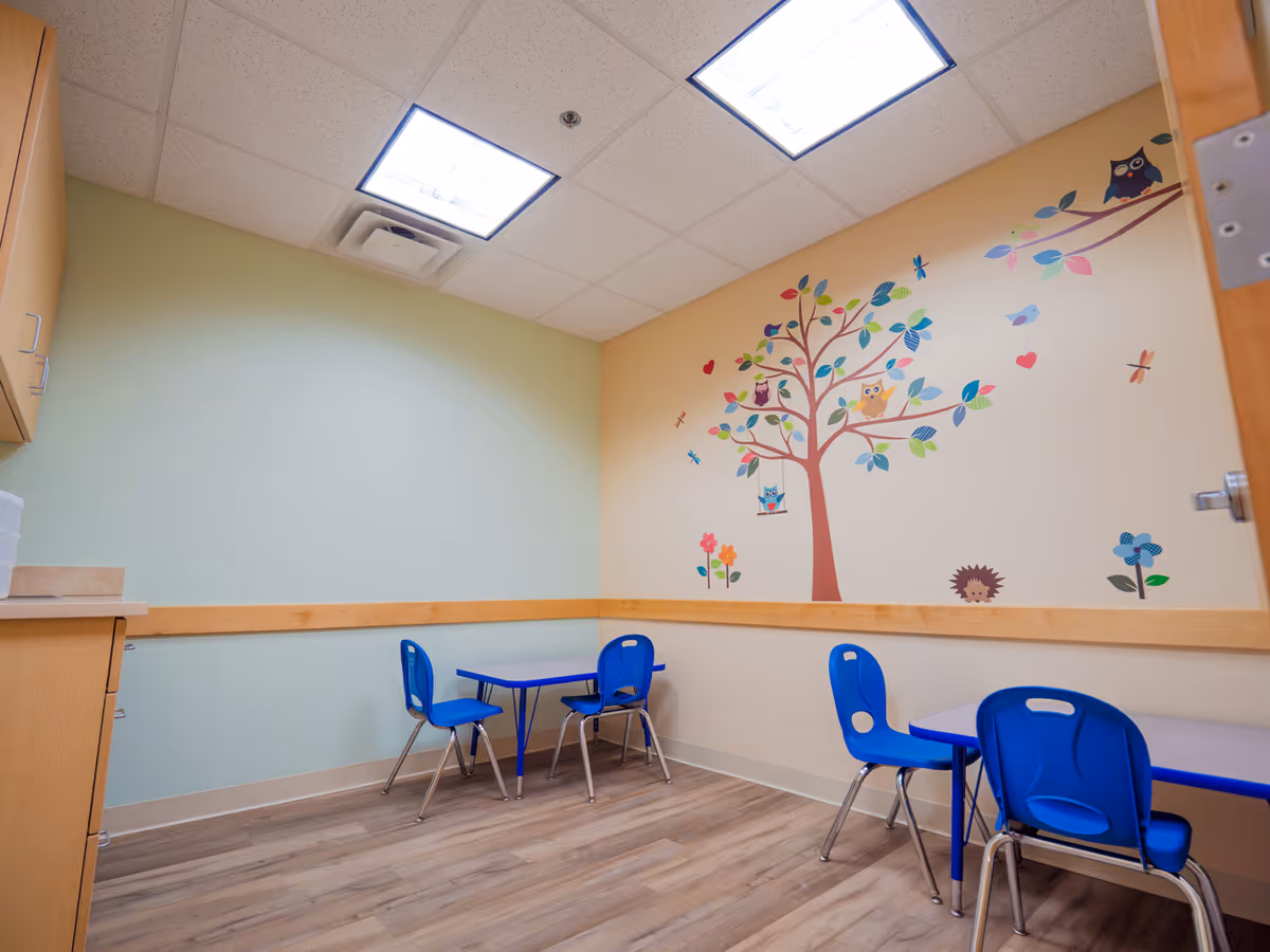 Colorful tree mural on wall with blue tables and chairs in a bright room.