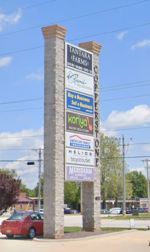 Tall stone sign with multiple business signs in a parking lot under a blue sky