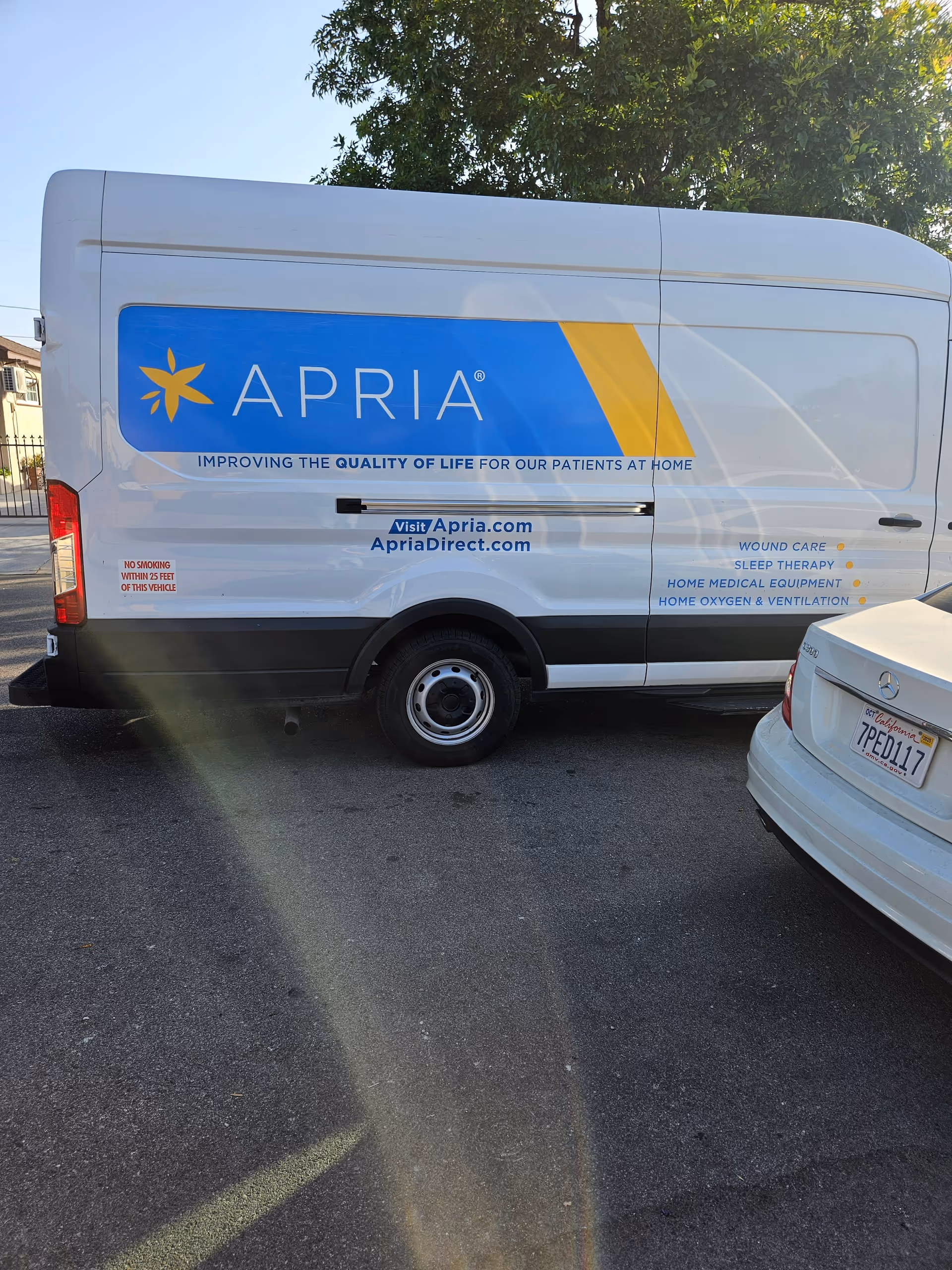 White Apria Healthcare van with blue and yellow branding parked in a lot.