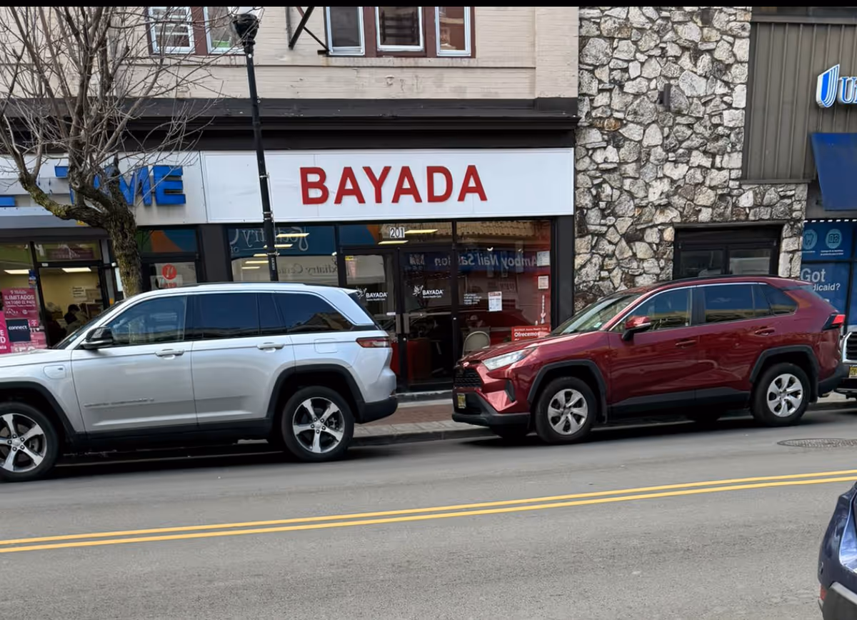 Storefront with a BAYADA sign, stone facade, and parked cars.