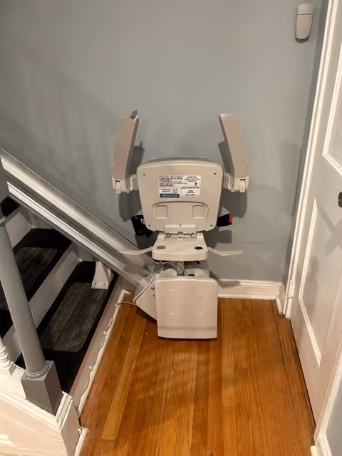 A stairlift device is installed beside a wooden staircase in a hallway.