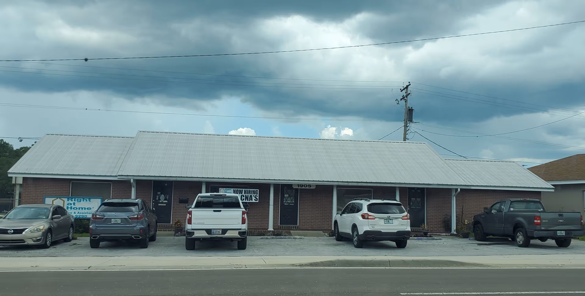 Front view of a single-story brick building with a metal roof and parked cars.
