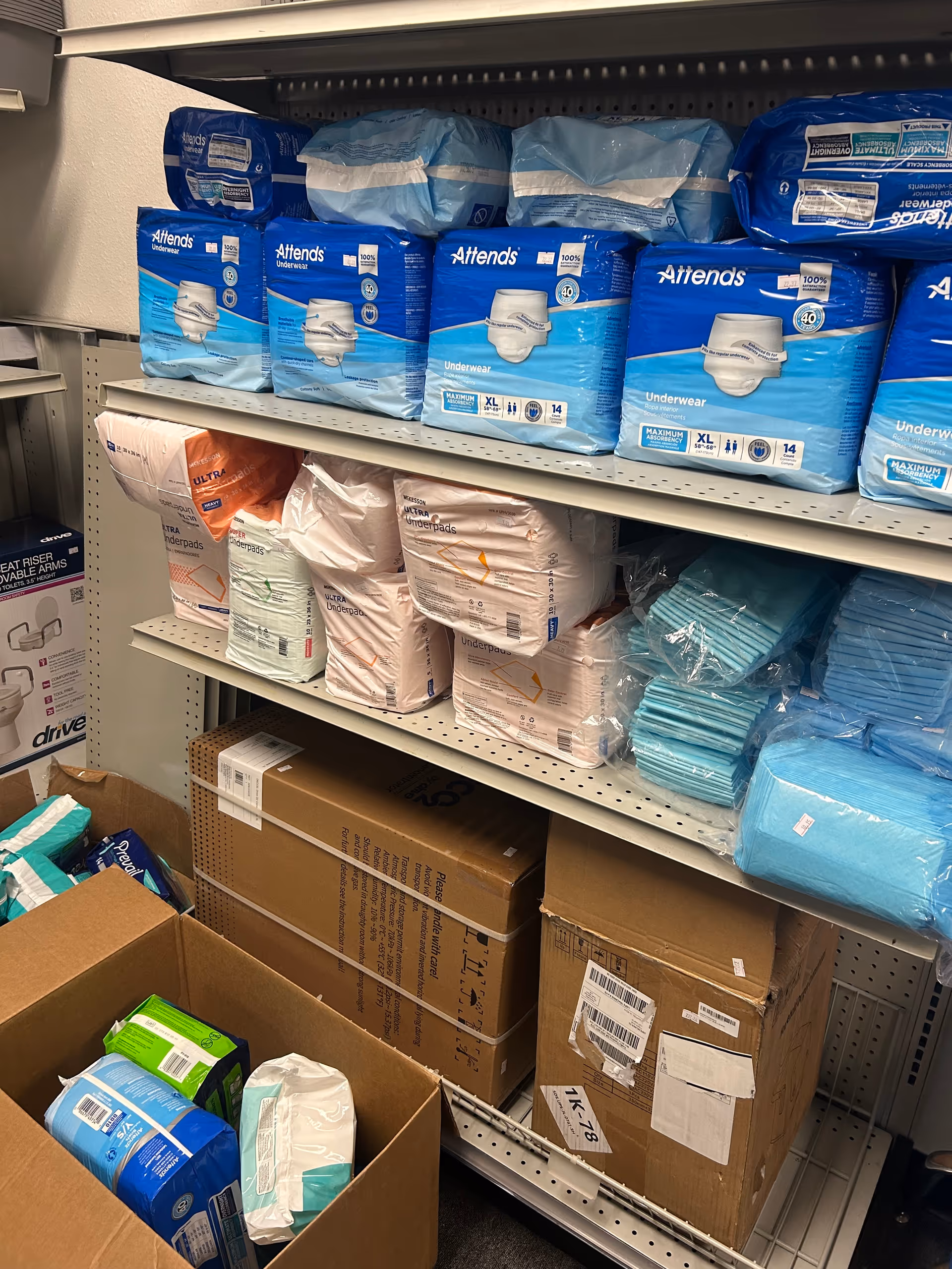 Shelves stocked with blue Attends incontinence products and cardboard boxes.