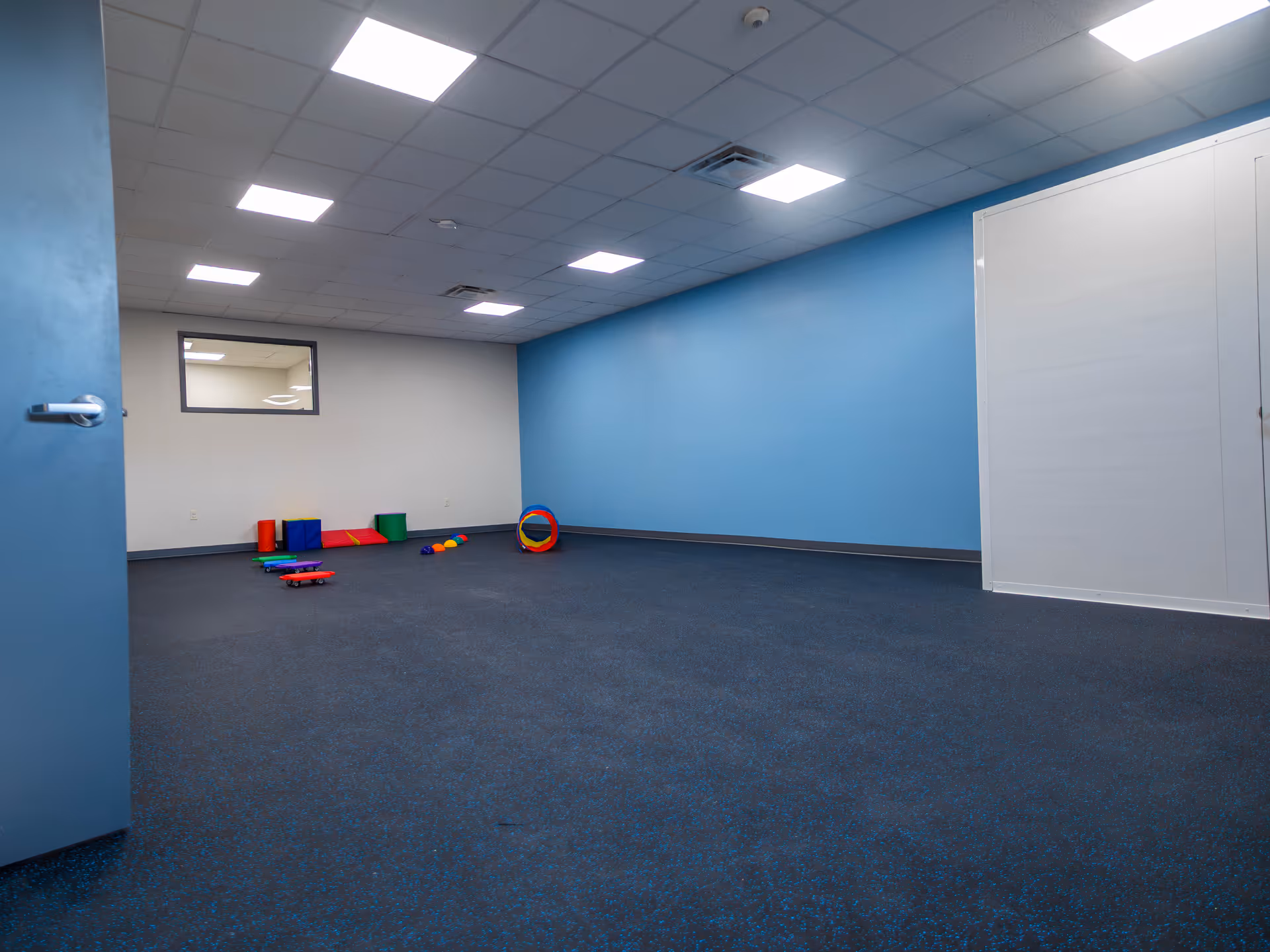 Interior room with blue walls, bright ceiling lights, and scattered colorful play equipment.