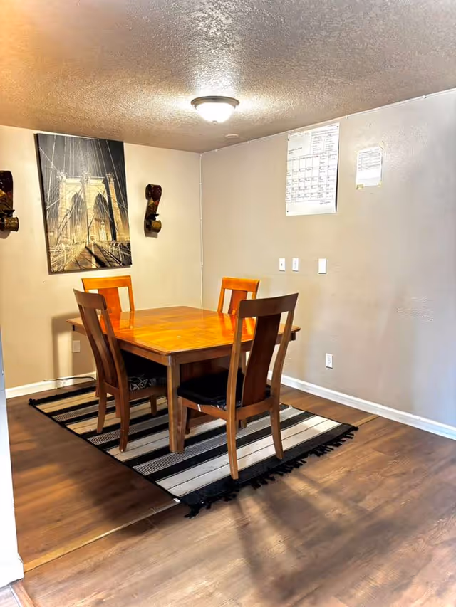 Wooden dining table with four chairs on a striped rug in a small dining area.