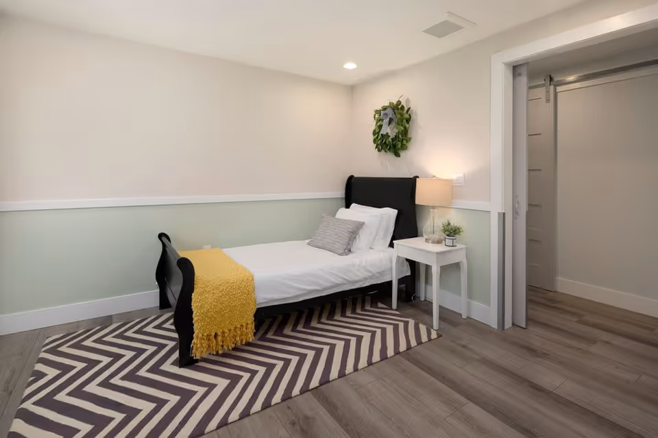 A tidy bedroom in a senior living facility with a single bed and bedside table.