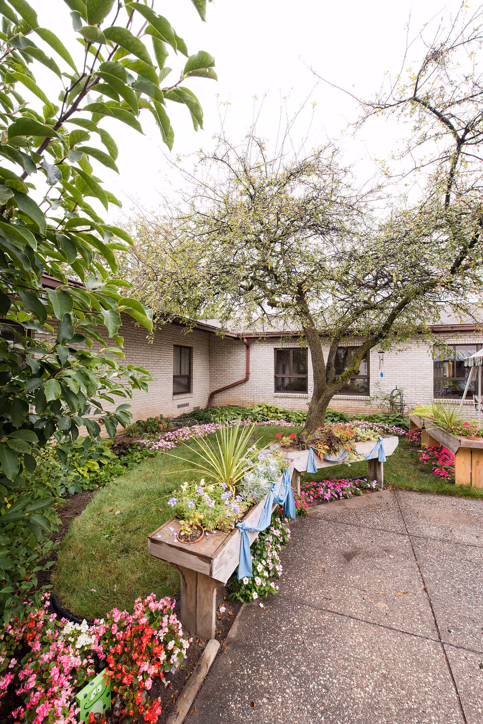 Outdoor courtyard with flowering planters along a walkway beside a brick building.