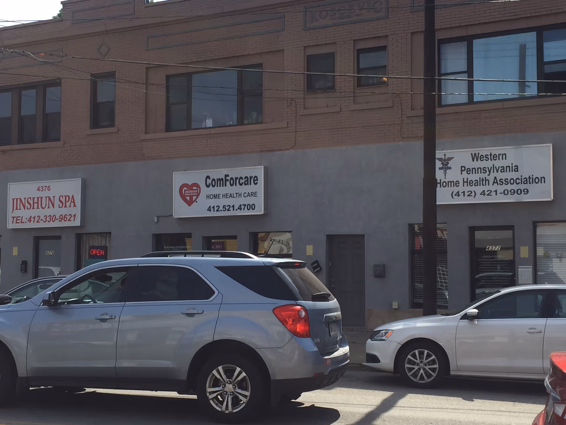 Exterior storefront with ComForCare signage and cars parked in front of shops.
