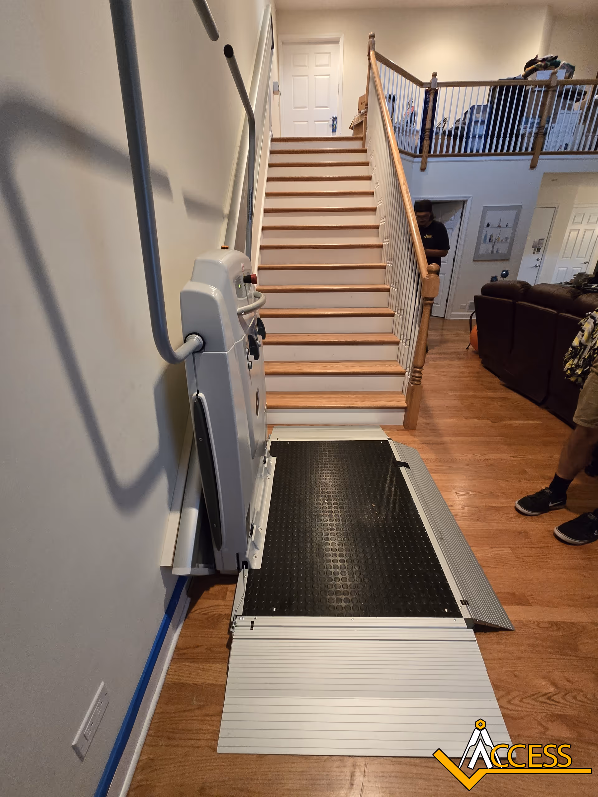 Indoor stairwell with a residential wheelchair lift and ramp beside the living room.