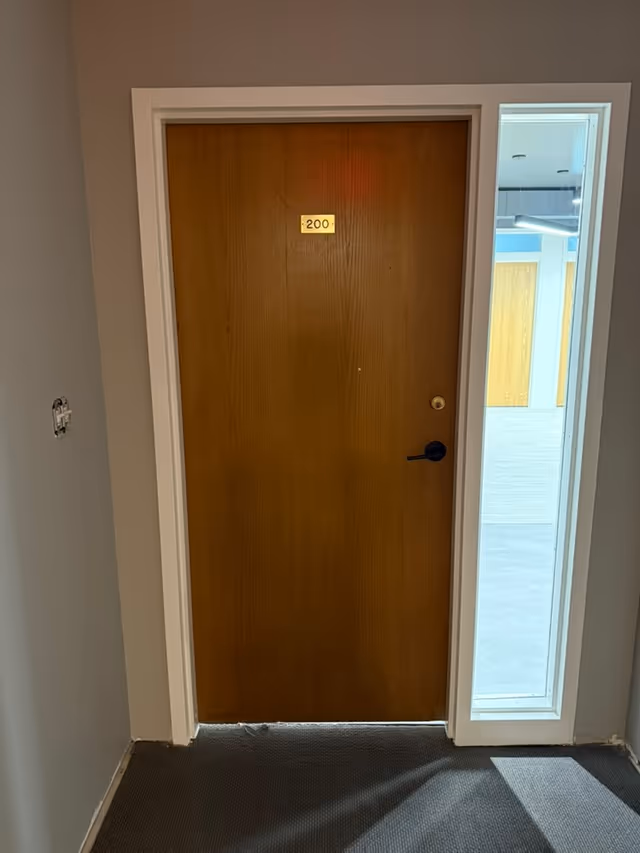 Wooden door labeled 200 in a hallway with a glass panel beside it.
