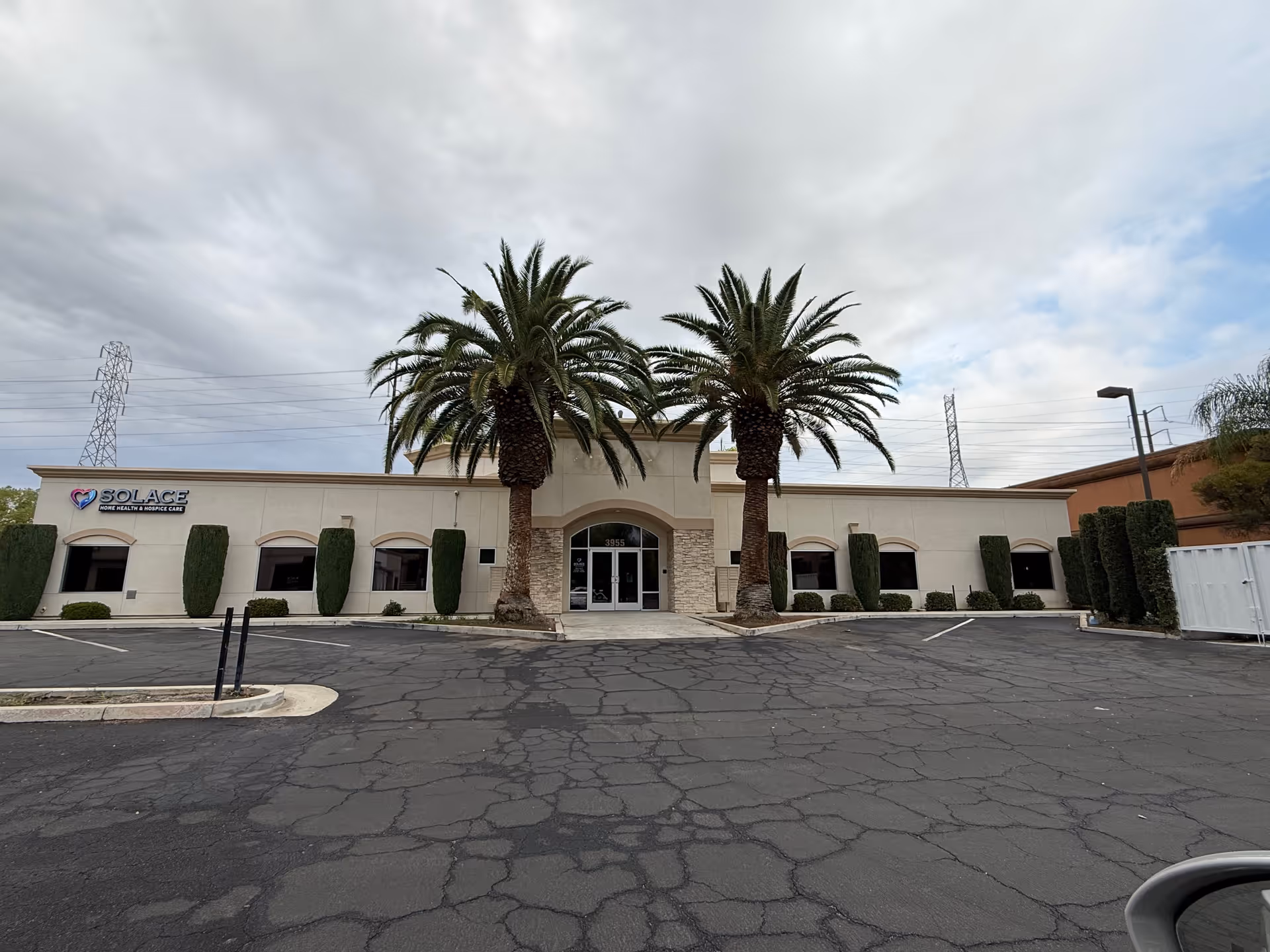 Single-story medical facility facade with palm trees, signage, and a large parking lot.