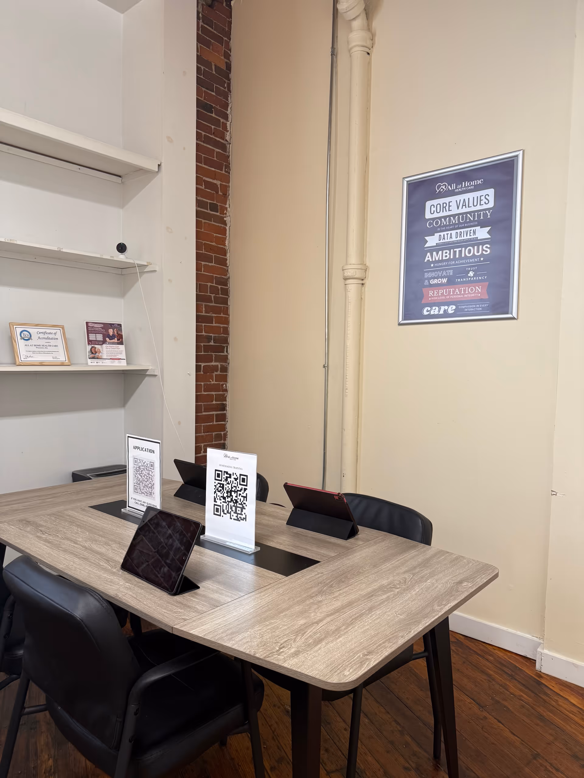 Interior meeting area with a wooden table, tablets, QR stands, shelves, and framed poster.